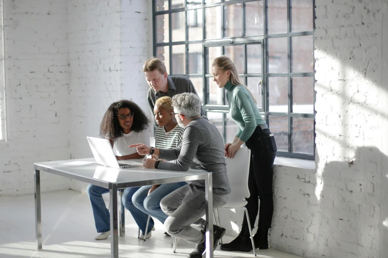 a group of people sitting around a table with a laptop, standing on a desk