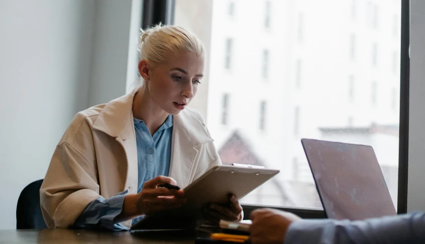 a woman sitting at a table using a tablet computer, pexels, medium shot of two characters, blonde, professional comercial vibe, thumbnail