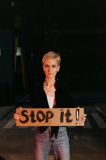 a woman holding a sign that says stop 14, an album cover, trending on pexels, feminist art, evan rachel wood, dark. no text, joel fletcher, in a menacing pose