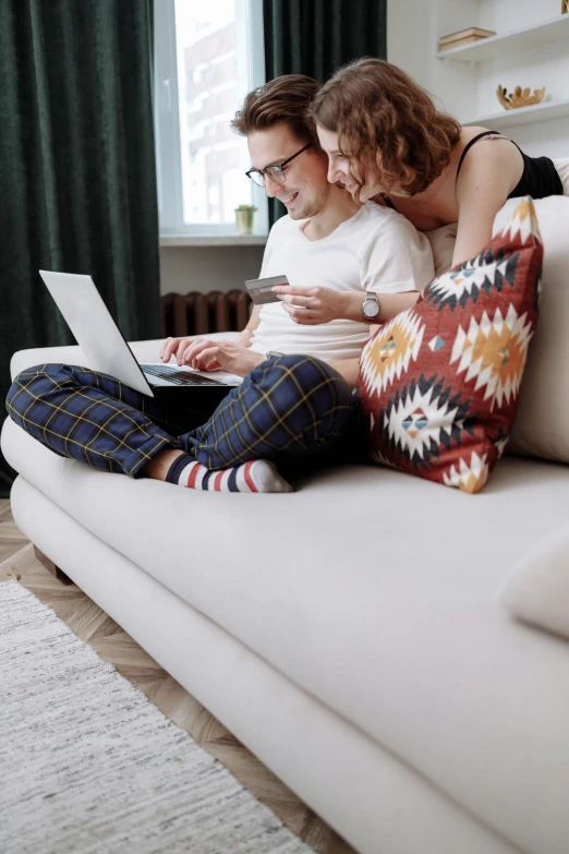 a man and woman sitting on a couch looking at a laptop, trending on pexels, sitting on the floor, lesbians, patterned, white l shaped couch