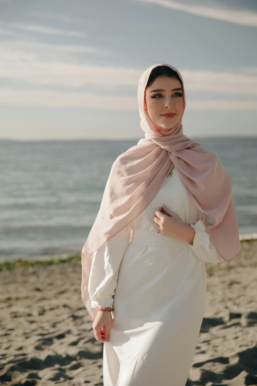 a woman standing on top of a sandy beach, inspired by Nazmi Ziya Güran, renaissance, light blush, wearing a scarf, at the waterside, formal wear