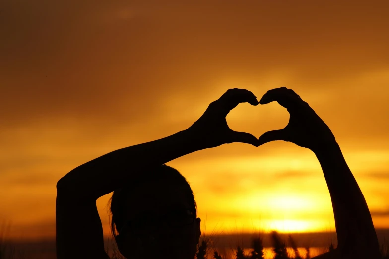 a person making a heart shape with their hands, pexels contest winner, sun behind her, avatar image, profile image, half body photo