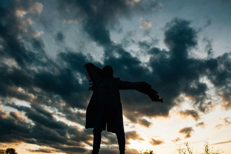 a silhouette of a person on a skateboard at sunset, a statue, pexels contest winner, happening, covered in clouds, wearing black clothes and cape, spreading her wings, looking towards camera