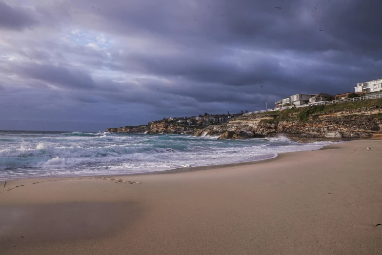 a large body of water sitting on top of a sandy beach, by Peter Churcher, pexels contest winner, bondi beach in the background, stormy lighting, coastal cliffs, early evening