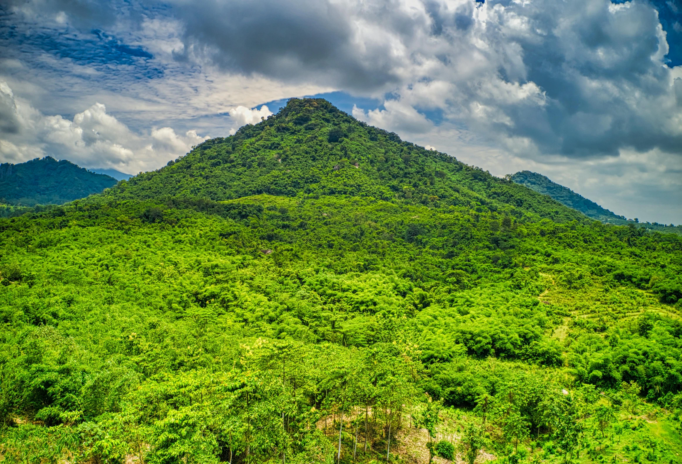 a mountain covered in lush green vegetation under a cloudy sky, drone photo, slide show, laos, conde nast traveler photo