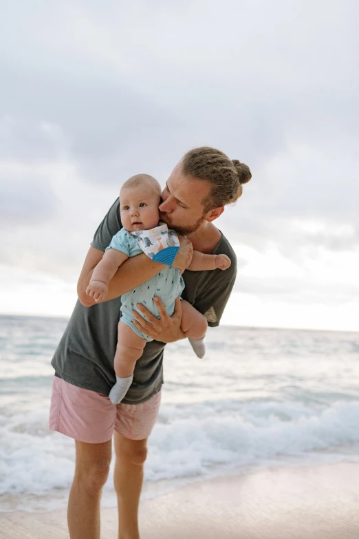 a man holding a baby on the beach, unsplash, maui, square, boys, bowater charlie and brom gerald