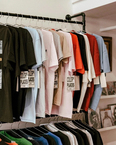 a bunch of shirts hanging on a rack, a cartoon, trending on unsplash, colorful signs, inspect in inventory image, t-shirt, non-binary
