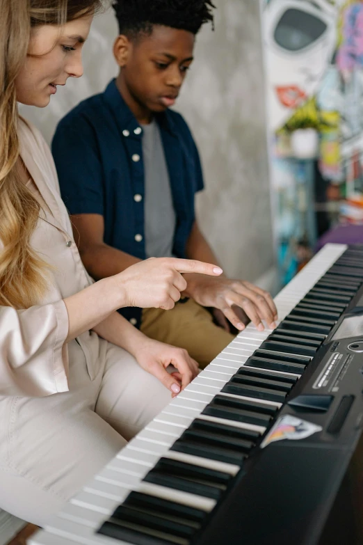 a woman sitting next to a boy playing a piano, trending on pexels, zoomed in, teaching, pastel', dynamic closeup