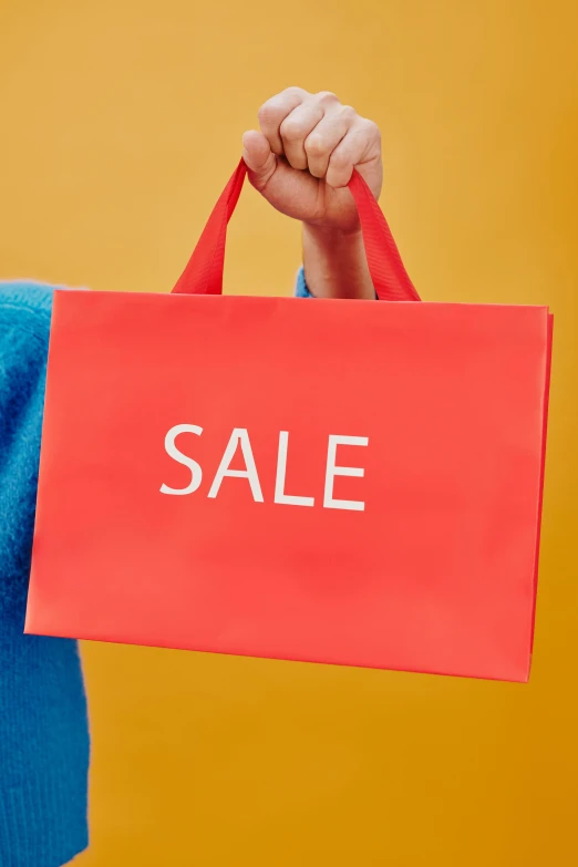 a woman holding a sale sign in front of her face, by Rachel Reckitt, dressed in red paper bags, thumbnail, close up image