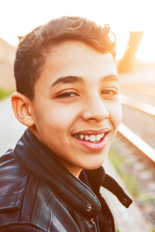 a close up of a person on a train track, teen boy, mutahar laughing, sun behind him, light skin tone