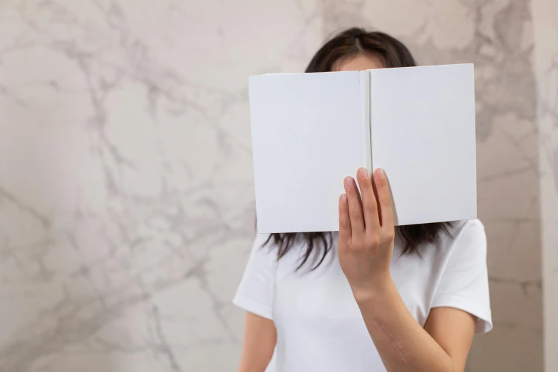 a woman covering her face with a book, an album cover, unsplash, made of all white ceramic tiles, background image, square face, high resolution photo