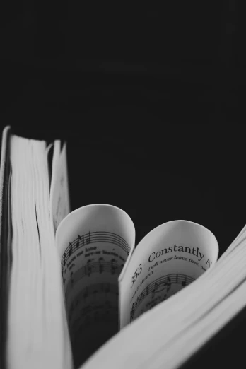an open book sitting on top of a table, a black and white photo, unsplash, sheet music, contorted, open books, dark backround