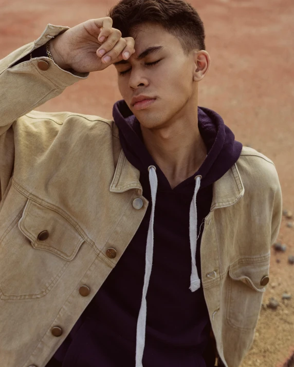 a man standing on top of a dirt field, an album cover, by Cosmo Alexander, trending on pexels, photorealism, beige hoodie, androgynous face, non binary model, pouting