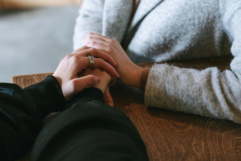 a man and a woman holding hands at a table, trending on pexels, background image, lesbian embrace, sitting in a waiting room, colour photograph