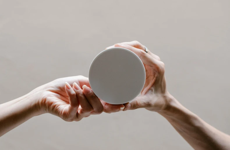 a person holding a white object in their hand, inspired by Jan Rustem, trending on pexels, metal lid, on grey background, light skin, round design