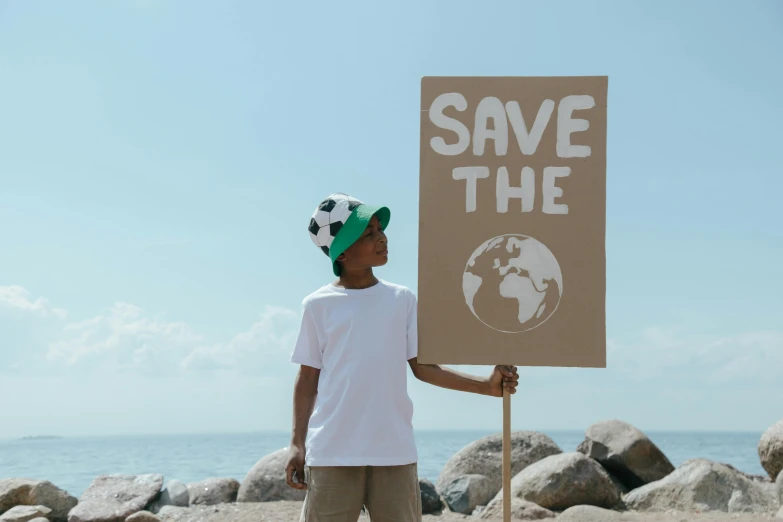 a man holding a sign that says save the earth, by Julia Pishtar, pexels contest winner, soccer, coastal, the little prince, modelling