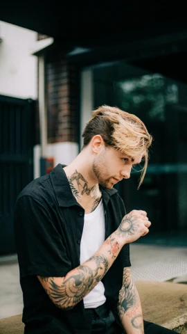a man with tattoos sitting on a ledge, an album cover, inspired by Cam Sykes, pexels contest winner, long swept back blond hair, profile image, headshot profile picture, androgynous male