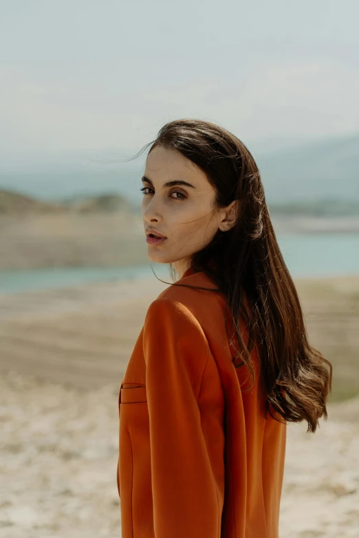 a woman standing on top of a sandy beach, by irakli nadar, pexels contest winner, long orange sweatshirt, sophisticated young woman, center parted brown hair, a mountain look like a women