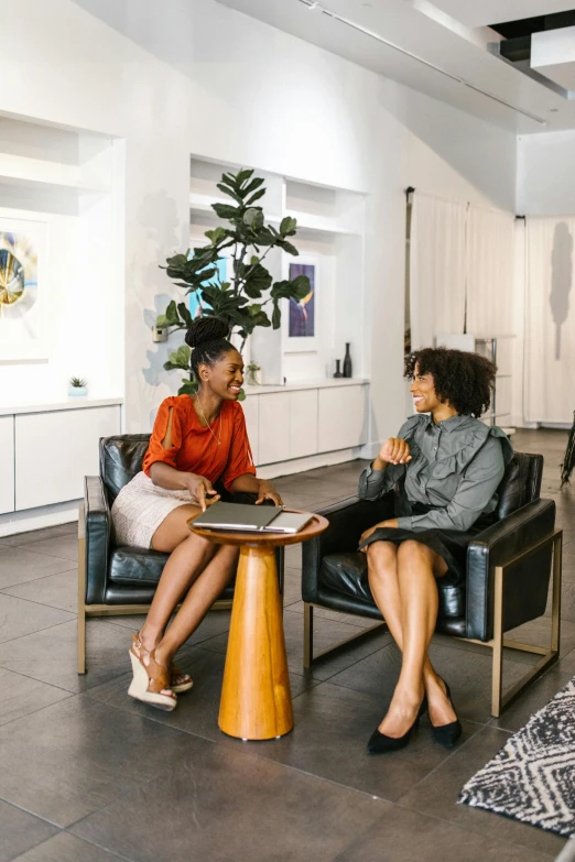 a couple of women sitting next to each other in a living room, by Gavin Hamilton, pexels contest winner, in a meeting room, photo of a black woman, vp of marketing, on a coffee table