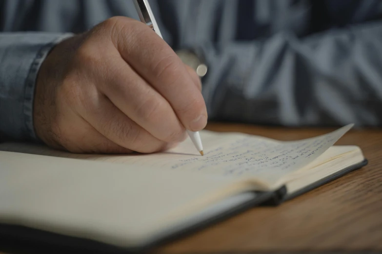 a person writing in a notebook with a pen, by David Simpson, cinematic, thumbnail, high quality image, lachlan bailey