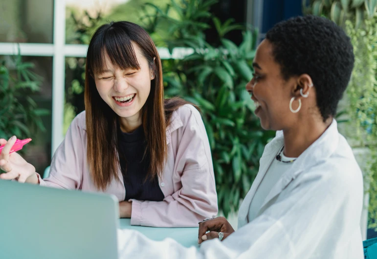 two women sitting at a table with a laptop, trending on pexels, ethnicity : japanese, she is laughing, healthcare worker, background image