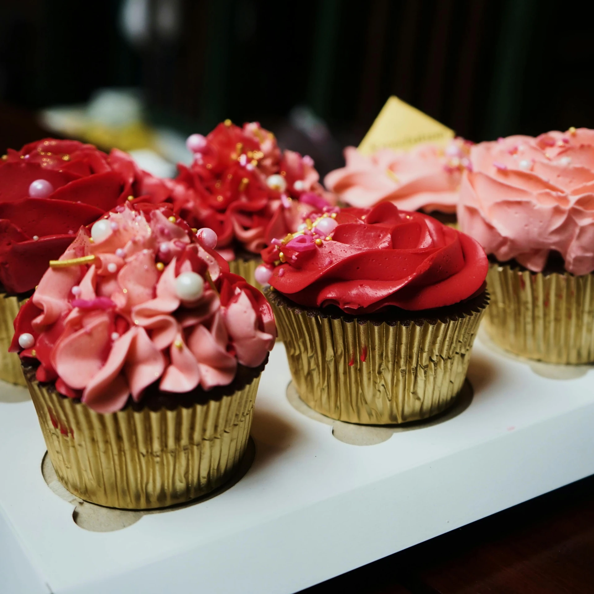 a row of cupcakes with pink frosting and sprinkles, pexels, red black and gold color scheme, instagram picture, fantasy bakery, wavy