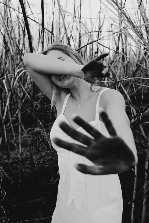 a black and white photo of a woman in a field, tumblr, aestheticism, hands shielding face, blood on clothes and face, palm body, in a swamp