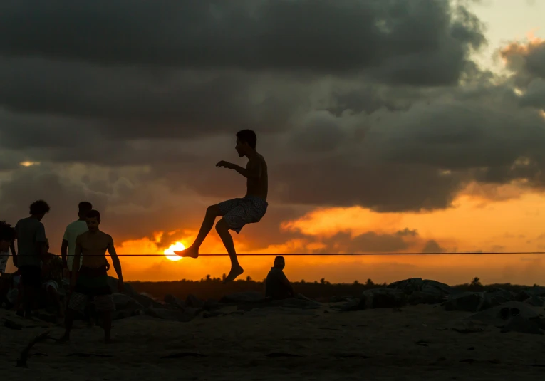 a group of people standing on top of a sandy beach, by Peter Churcher, pexels contest winner, flying through sunset, male calisthenics, playing soccer at the beach, dancing on a pole