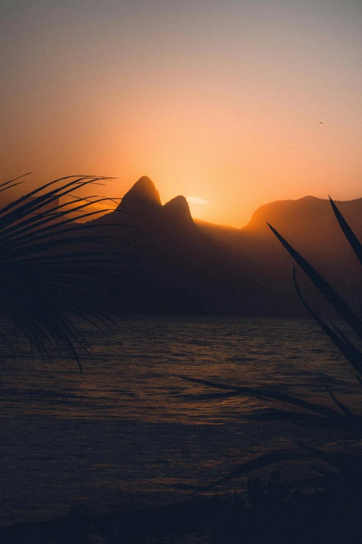 a sunset over a body of water with a mountain in the background, brazil, palm, multiple stories, uploaded