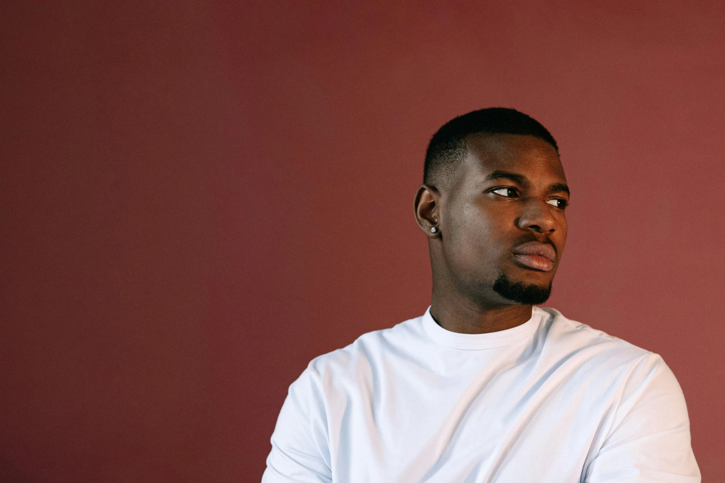 a man standing in front of a red wall, an album cover, inspired by Paul Georges, pexels contest winner, realism, maria borges, light stubble with red shirt, an all white human, looking from side!