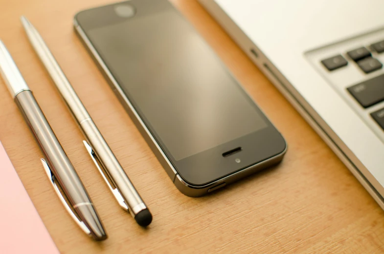 a cell phone sitting on top of a desk next to a laptop, by Niko Henrichon, pencils, feature, profile image, iphone