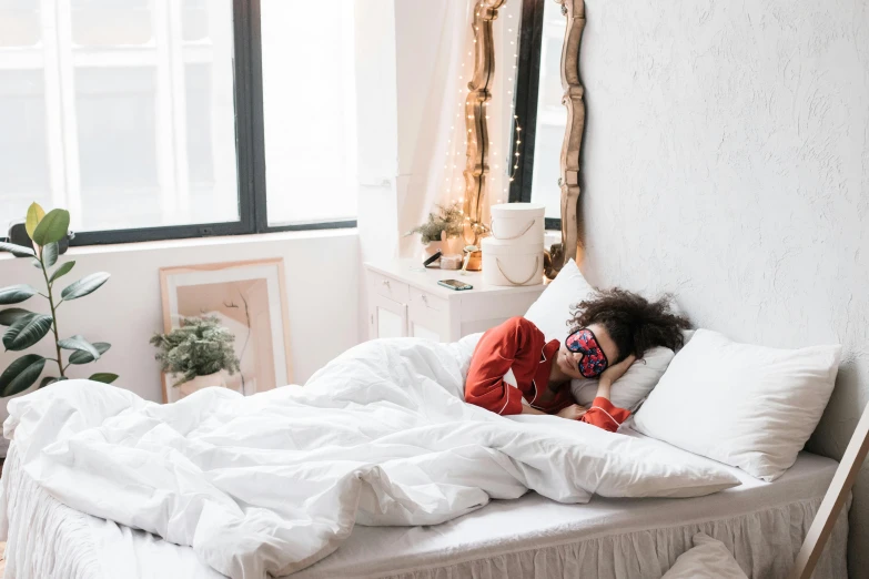 a woman laying on top of a bed next to a window, trending on pexels, wearing a mask, white and red color scheme, inside a cozy apartment, woman with rose tinted glasses