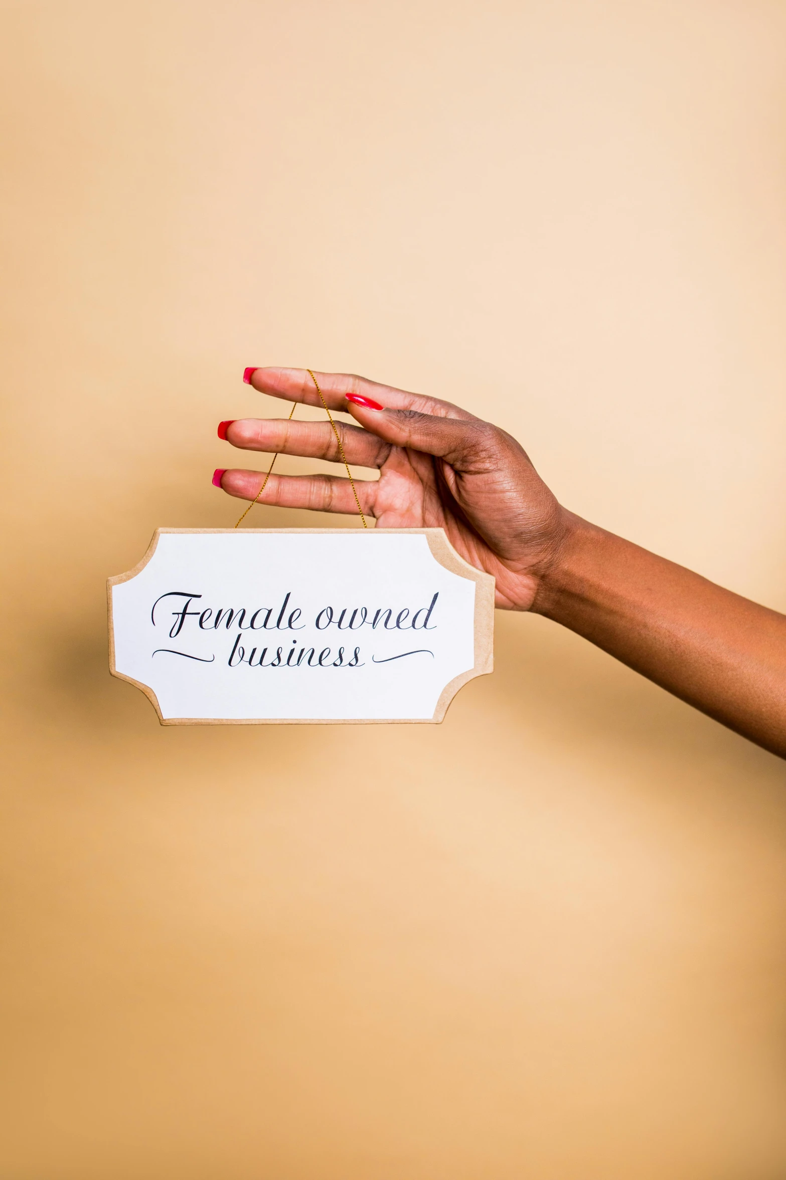 a woman holding a sign that says female owned, by Will Ellis, trending on pexels, plain background, essence, thumbnail, manicured