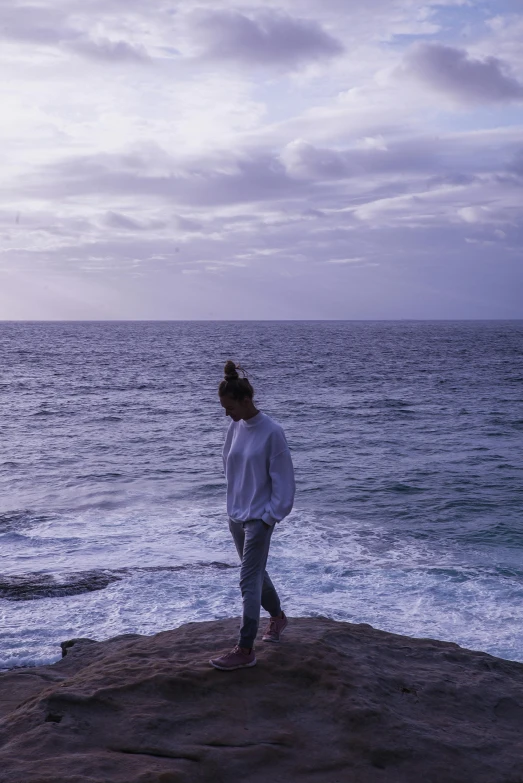 a woman standing on top of a rock next to the ocean, happening, purple head, manly, slightly minimal, 2019 trending photo