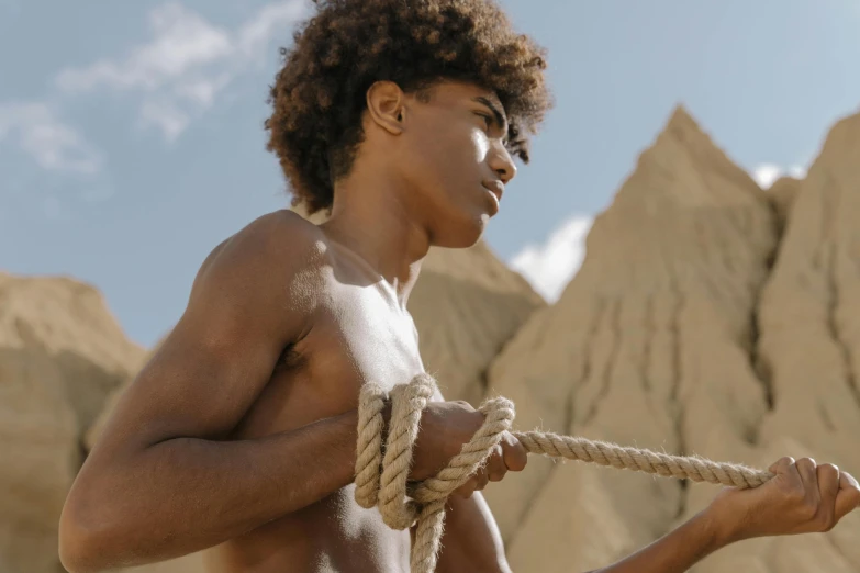 a shirtless young man holding a rope, trending on pexels, afrofuturism, 14 yo berber boy, brown, ashteroth, upper body image