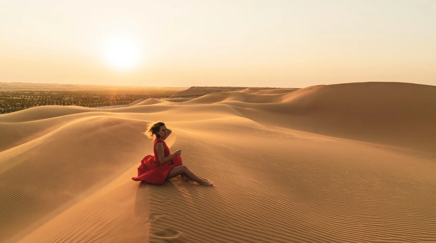 a woman in a red dress sitting on a sand dune, pexels contest winner, arabesque, desert oasis, looking towards the horizon, golden hues, instagram post