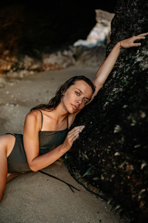 a woman sitting on a beach next to a rock, wet shiny skin, in a tree, profile image, swimsuit