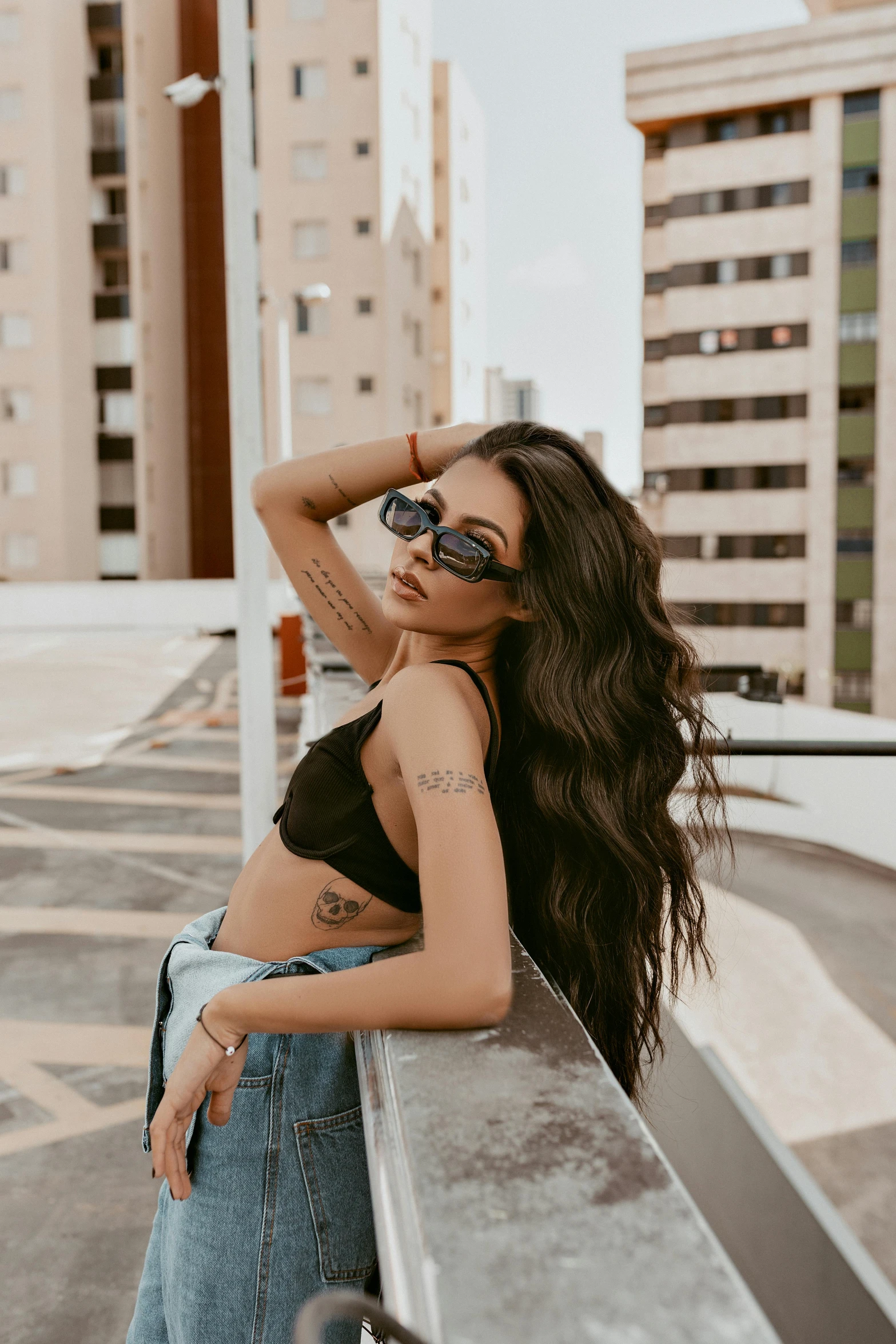 a woman standing on top of a roof next to tall buildings, inspired by Elsa Bleda, trending on pexels, graffiti, wavy long black hair and glasses, brazilan supermodel, croptop, hair : long brown