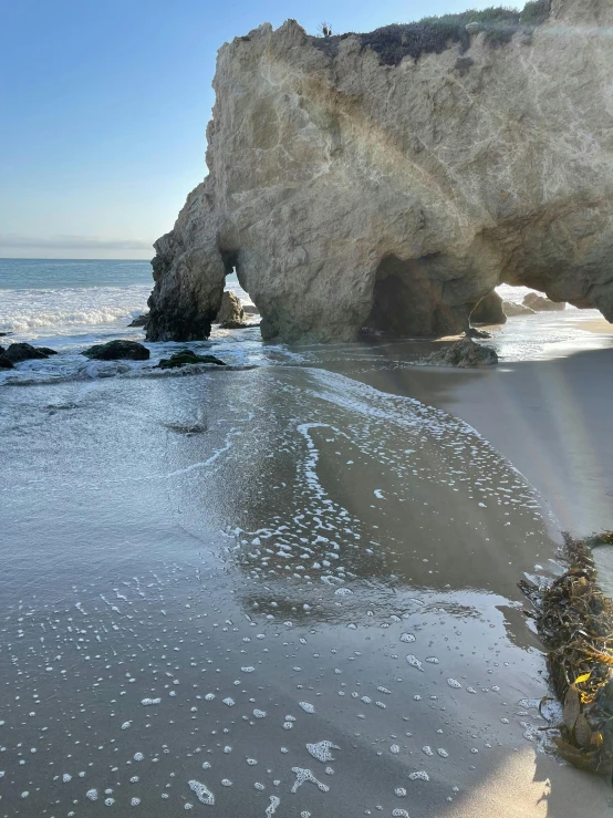 a person riding a surfboard on top of a sandy beach, caves, ethereal white dripping tar, archway, slide show