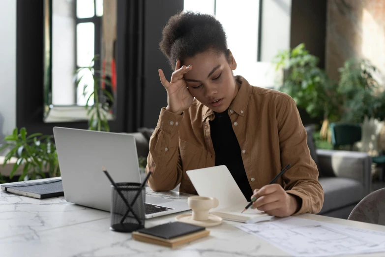 a woman sitting at a table with a laptop and papers, a cartoon, trending on pexels, renaissance, devastated, black young woman, professional photo, brown