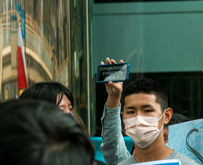 a man in a face mask holding up a cell phone, a picture, flickr, subject action : holding sign, hou china, onlookers, snapchat photo