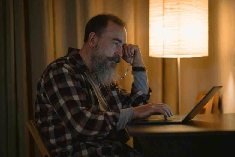 a man sitting at a desk using a laptop computer, a portrait, inspired by Ásgrímur Jónsson, pexels contest winner, grizzled beard, low light cinematic, 2 5 6 x 2 5 6 pixels, looking distracted