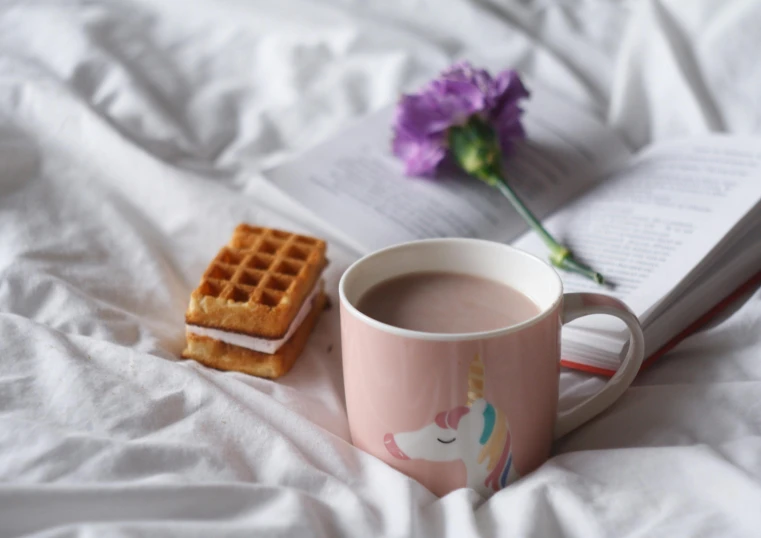 a book sitting on top of a bed next to a cup of coffee, inspired by Muggur, trending on pexels, magic realism, marshmallow graham cracker, pink pastel, white unicorn, on grey background