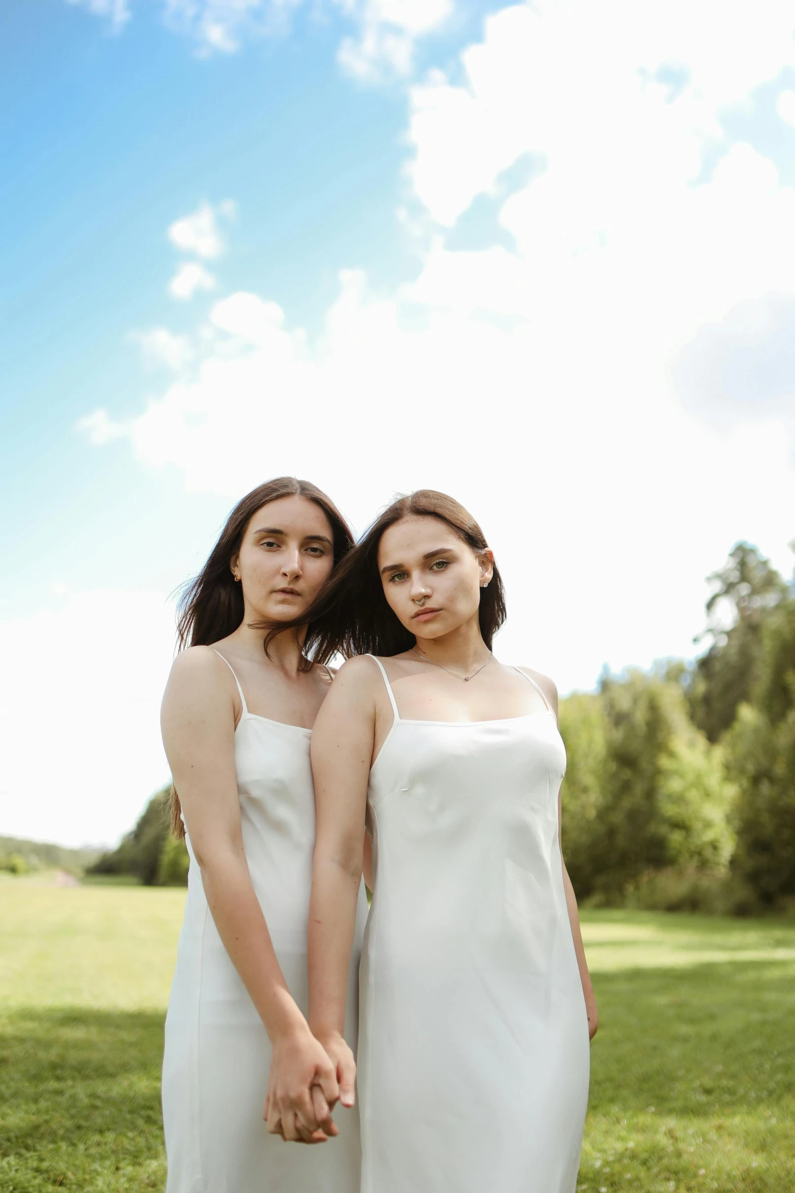 two women standing next to each other in a field, an album cover, by Julia Pishtar, trending on pexels, wearing white camisole, porcelain white skin, portrait shot 8 k, soft silk dress