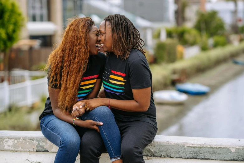 a couple of women sitting next to each other, unsplash, pride month, wearing a t-shirt, beautiful city black woman only, couple kissing