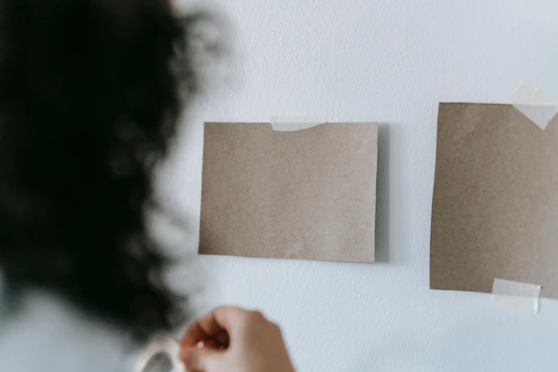 a woman putting pieces of paper on a wall, pexels contest winner, wearing a brown, minimalist sticker, holding it out to the camera, profile image