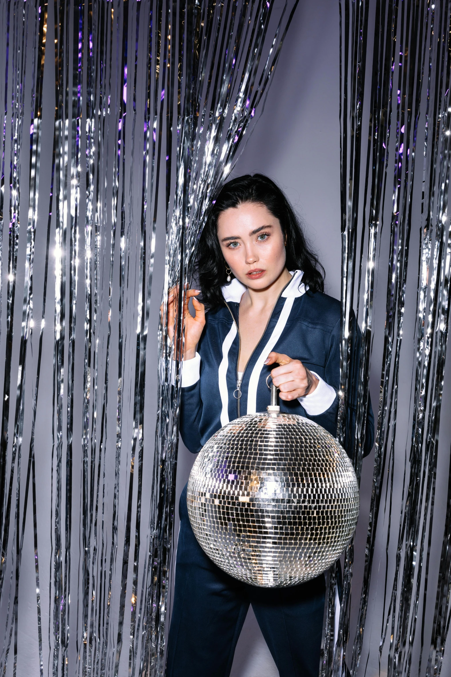 a woman holding a disco ball in front of a curtain, an album cover, by Julia Pishtar, trending on pexels, she has black hair, in a nightclub, lilly collins, 15081959 21121991 01012000 4k