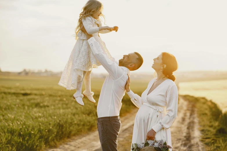 a man holding a little girl up in the air, pexels contest winner, renaissance, wearing a cute white dress, husband wife and son, evening sun, unique design