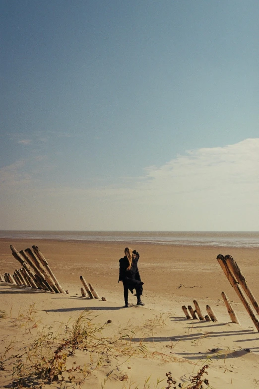 a couple of people standing on top of a sandy beach, inspired by Henri-Julien Dumont, unsplash, romanticism, dunkirk, fences, color film still, tim walker