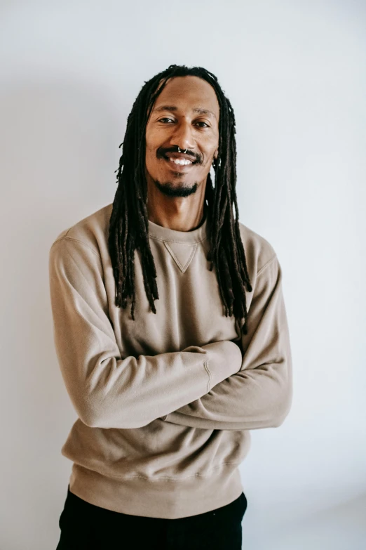 a man with dreadlocks standing with his arms crossed, he is wearing a brown sweater, jordan lamarre - wan, tall and thin, kano)
